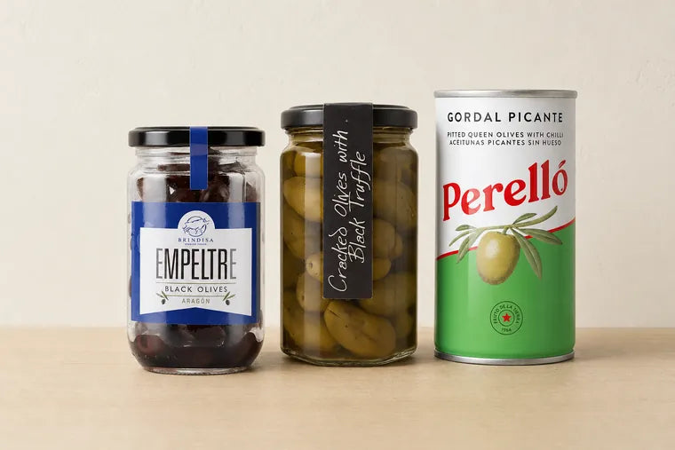 Three jars from the olive shelf: Brindisa Empeltre black olives from Aragón, a hand-labelled jar of cracked olives with black truffle, and a tin of Perelló Gordal Picante queen olives.