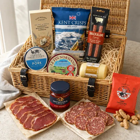 An open wicker basket packed with Kent crisps, pork pâté, Camembert and chorizo, sliced charcuterie laid out in front.