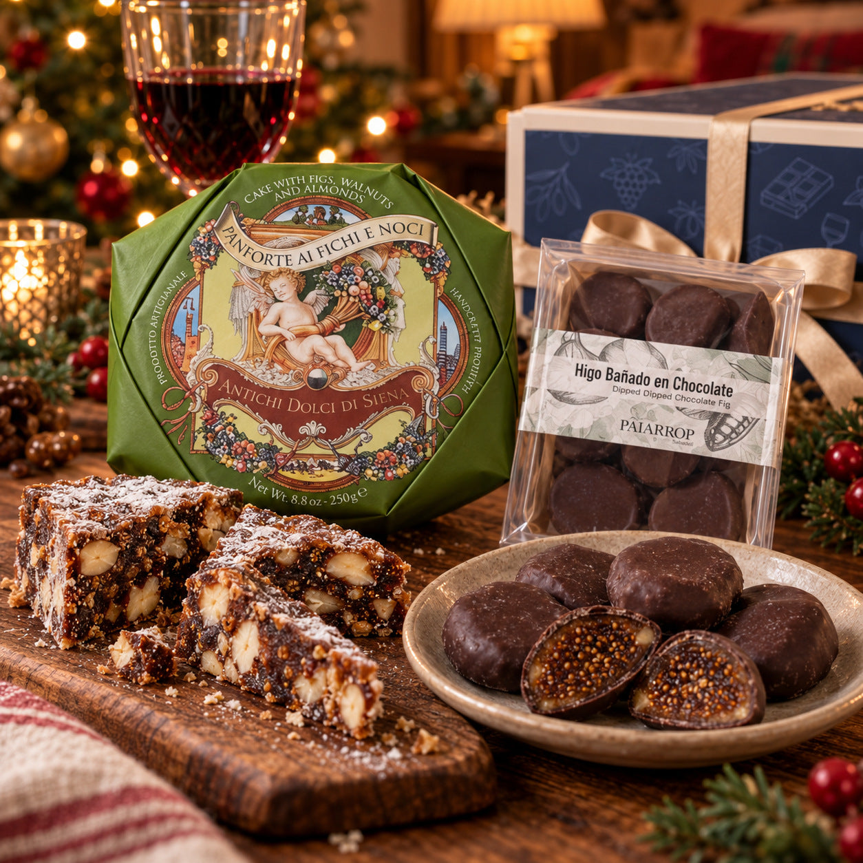 Detail from The Christmas Cheeseboard: fig and walnut panforte cut into slices beside its green wrapper, and dark chocolate dipped figs on a small plate, one cut in half.